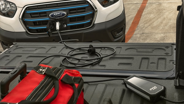Ford E-Transit blanca  cargándose, con cargador portátil en la batea  de una pickup.